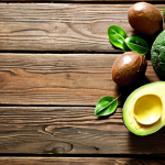 **Brain Fuel:** A vibrant still life featuring avocados, olive oil, almonds, and leafy green vegetables arranged on a rustic wooden table. Sunlight streams in, highlighting the textures and colors of the healthy fats and nutrient-rich foods. The overall mood is one of energy and cognitive clarity.
